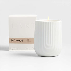 A white porcelain candle holder with vertical ridges is lit from within, showcasing a warm glow. Next to it is its packaging box with the brand name 'Lanterne' visible on it.